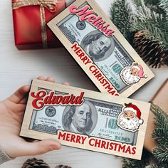 two wooden christmas cards with santa claus and money on them, sitting next to pine cones