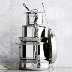 a stack of pots and pans sitting on top of a counter next to utensils