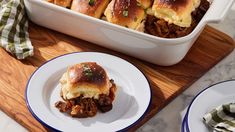 a casserole dish filled with pulled pork and cheese rolls on a wooden cutting board