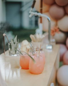 three glasses filled with drinks sitting on top of a table next to balloons and flowers