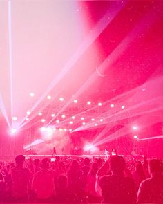 a large group of people standing on top of a stage with bright pink lights above them