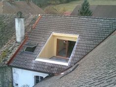 an open window on the roof of a building with rooftoping shingles and trees in the background