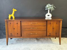 a wooden sideboard with three drawers and a yellow toy giraffe on top