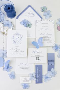 the wedding stationery is laid out on top of each other with blue flowers and butterflies