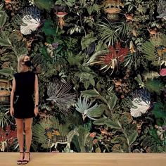 a woman standing in front of a wall with plants on it