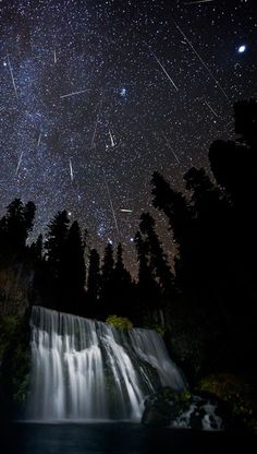 the night sky is filled with stars above a waterfall