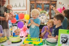 a group of children standing around a table with cake and balloons in the air above them