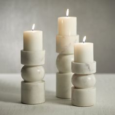 three white candles are stacked on top of each other, with one candle lit in the middle