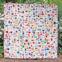 a colorful quilt is displayed in front of some trees