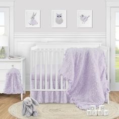 a baby crib with purple bedding and pictures on the wall above it, along with a stuffed animal