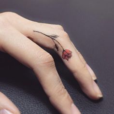 a woman's hand with a red flower tattoo on her left thumb and finger