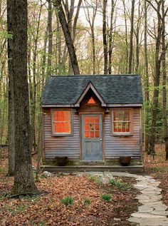 a small wooden cabin in the woods surrounded by trees and leaves, with a pathway leading to it