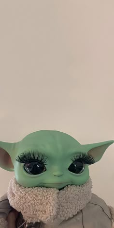 the child yoda doll has long eyelashes and is wearing a white coat with a fur collar