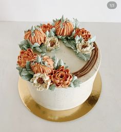 a cake decorated with flowers and leaves on a gold plated platter, sitting on a white surface