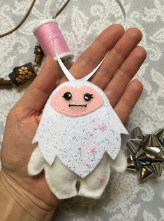 a hand holding an ornament with a face on it and two spools of thread in the background