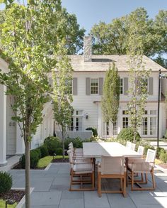 an outdoor dining table and chairs in front of a large white house