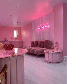 a room with pink walls and furniture in the center is lit up by neon lights