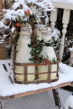 some bottles are sitting in the snow on a bench with holly and berries around them