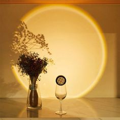 a vase with flowers and a wine glass sitting on a table in front of a wall