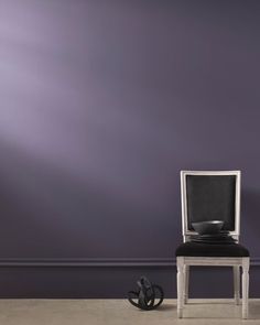 a chair with a bowl on it sitting in front of a purple wall next to a black object