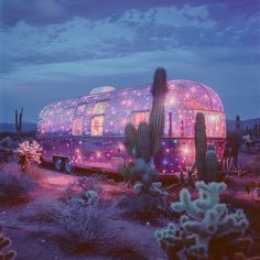 an airstream is lit up in the desert with cactus and cacti around it