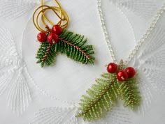 two necklaces with red berries and green leaves hanging from them on a white tablecloth