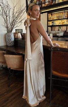 a woman standing in front of a bar with her back to the camera and wearing a dress