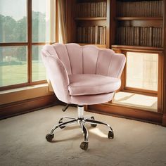 a pink chair sitting in front of a window next to a book shelf filled with books