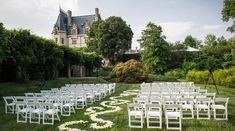 an outdoor ceremony set up with white chairs and flowers on the grass in front of a castle