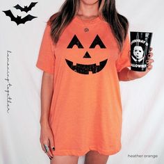 a woman wearing an orange halloween shirt holding a black coffee mug in her right hand