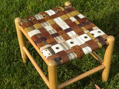 a small wooden stool made out of leather and wood strips on grass with leaves around it