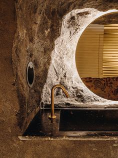 a sink in front of a stone wall with a round mirror on it's side