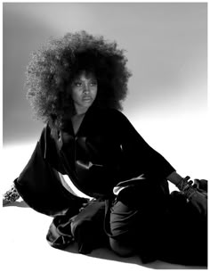 a woman sitting on the ground with an afro hairstyle and black dress, posing for a photo