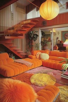 a living room filled with lots of orange couches next to a stair case and table