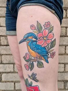 a colorful bird sitting on top of a tree branch with flowers and leaves around it