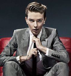 a man in a suit sitting on a red chair with his hand under his tie