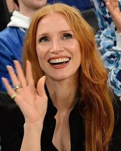 a woman with red hair is smiling and raising her hand in front of the camera