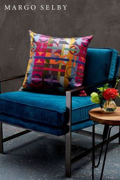 a blue chair sitting next to a table with flowers on top of it in front of a gray wall