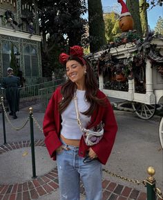 a woman standing on the sidewalk in front of a horse drawn carriage wearing a red bow