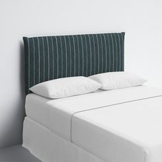 a bed with white pillows and green headboard against a white wall in an empty room