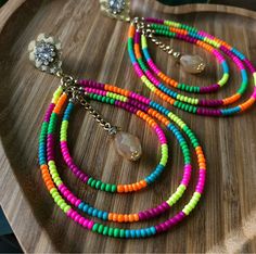 multicolored beaded necklace and earring set on a wooden platter with crystal brooches