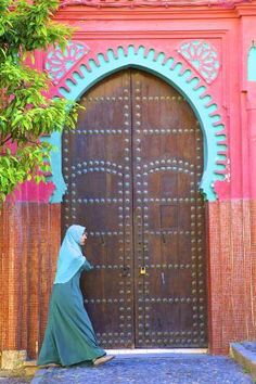 a woman in a hijab is standing by a large wooden door with intricate carvings on it