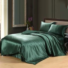 a bed with green sheets and pillows in a room next to a lamp on a table