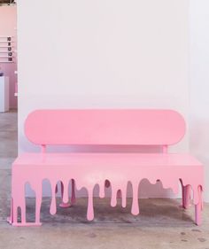 a pink bench sitting in front of a white wall with paint dripping down it's sides