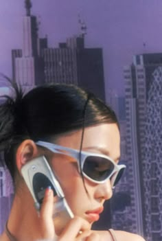 a woman wearing sunglasses talking on a cell phone in front of a cityscape