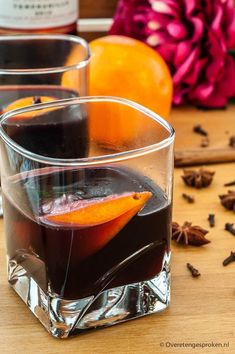 two glasses filled with liquid sitting on top of a wooden table next to an orange