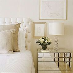 a white bedroom with mirrored nightstands and pictures on the wall above it, along with a bed