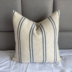 a white and blue striped pillow sitting on top of a gray headboard next to a bed