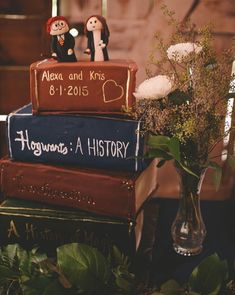 a stack of books sitting next to a vase filled with flowers and two figurines on top of them