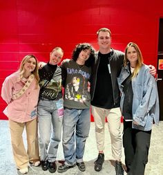 a group of young people standing next to each other in front of a red wall